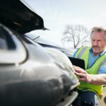 Mature Male Loss Adjuster With Digital Tablet Assessing Insurance Claim In Car Pound