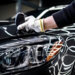 Technician Measuring Car Paint Near Headlight